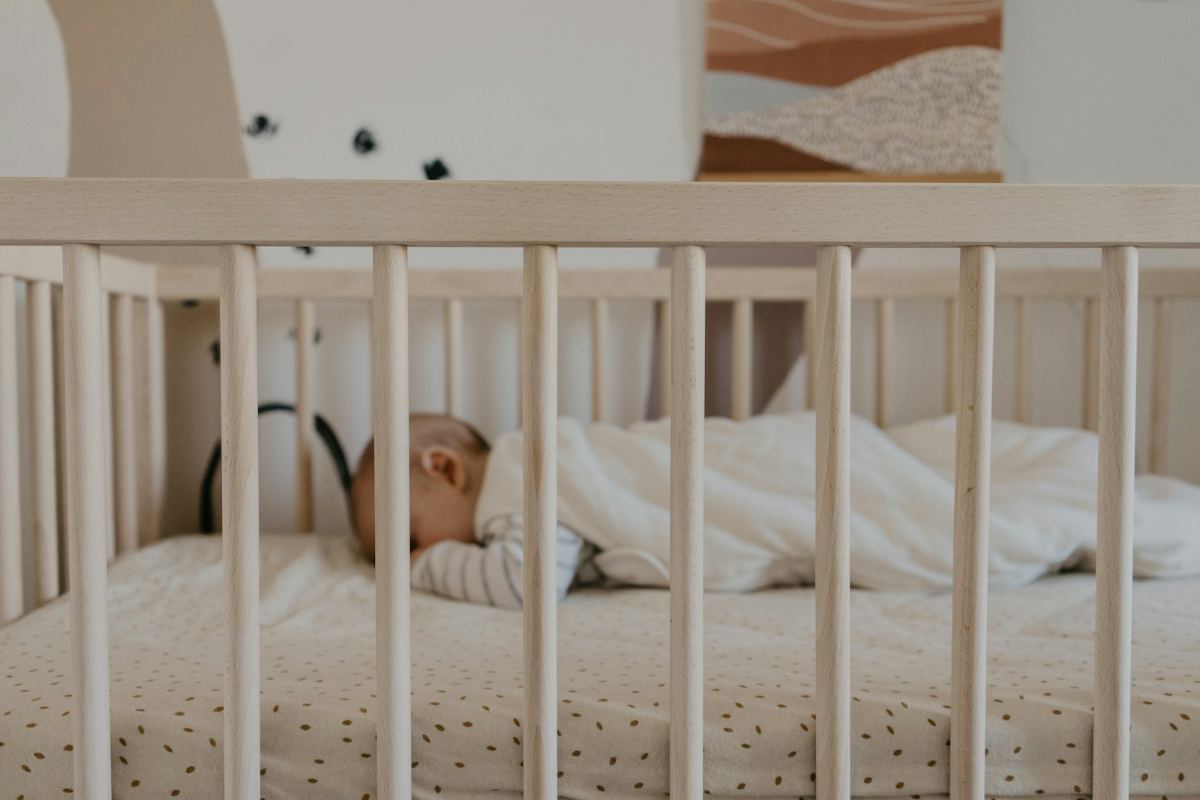 Un bebé duerme en una cuna de madera clara, en una habitación de tonos crema